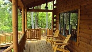 A wooden deck with two Adirondack chairs and a wooden railing overlooking a forest. - Spotted Fawn Cabin - Serenity and luxury await you (Shenandoah)