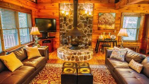 A cozy cabin interior with a stone fireplace, leather sofas, and a television. - Spotted Fawn Cabin - Serenity and luxury await you (Shenandoah)