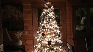 A Christmas tree in a wooden cabin with a white base and lights. - Spotted Fawn Cabin - Serenity and luxury await you (Shenandoah)