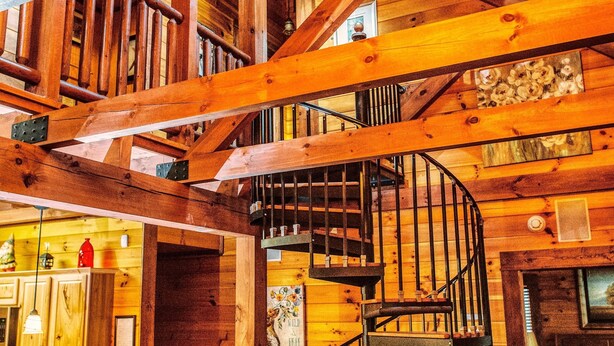 A wooden interior with a spiral staircase, wooden beams, and a kitchen area. - Spotted Fawn Cabin - Serenity and luxury await you (Shenandoah)