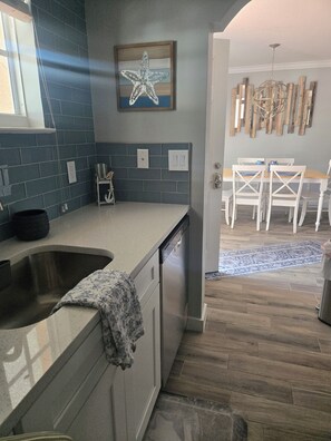 Cucina con lavastoviglie integrata, lavello e decorazione a stella marina sul muro. Si nota anche un'area pranzo con tavolo e sedie sullo sfondo.