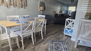 A dining area with a wooden table and white chairs, a patterned rug, and a ceiling fan.