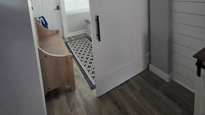 A hallway with a white door, a wooden bench, and a patterned rug.