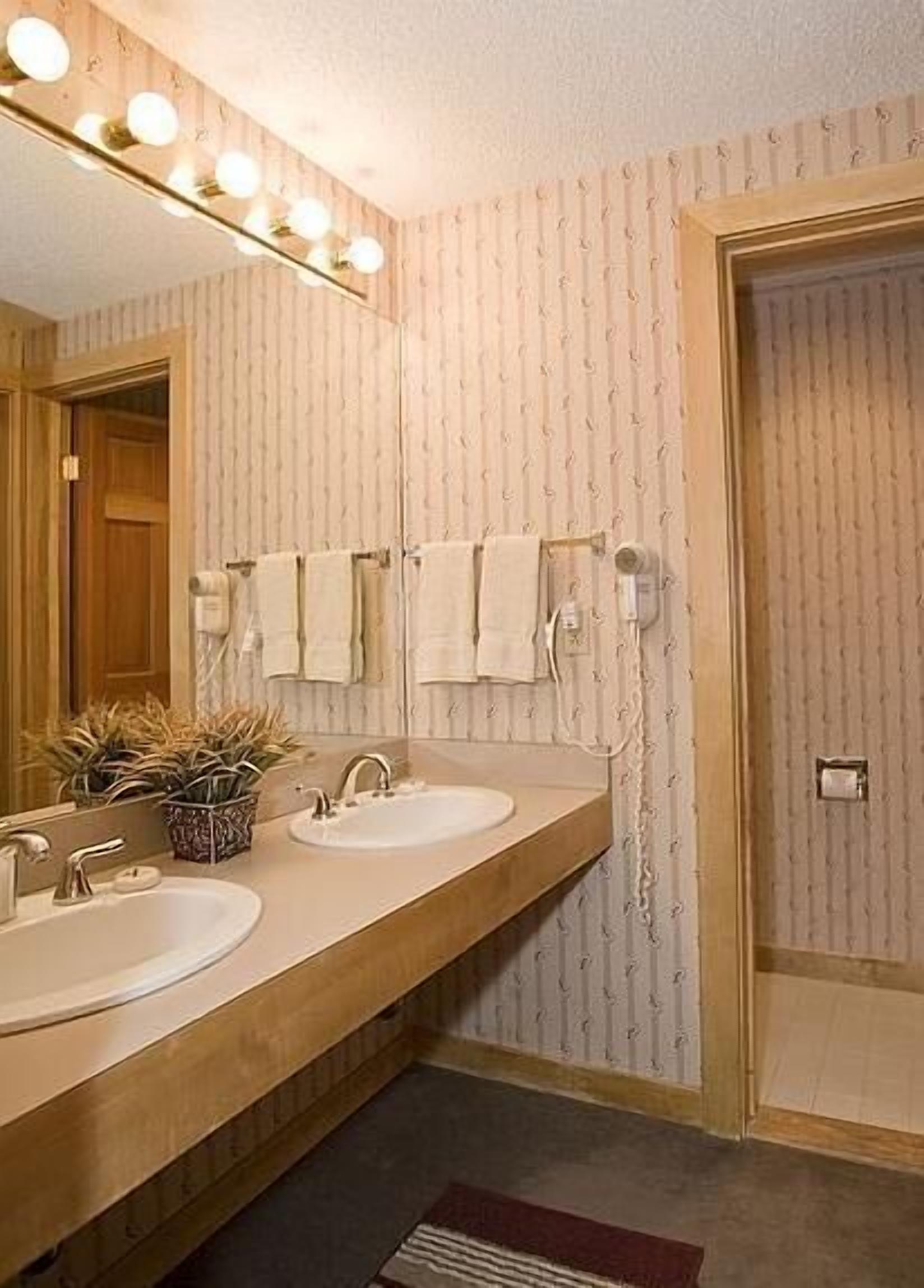 A bathroom with two sinks, a mirror with lights, and a towel rack.