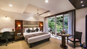 Une chambre d’hôtel moderne dotée d’un grand lit, d’un bureau, d’une chaise et d’un balcon offrant une vue sur la verdure.