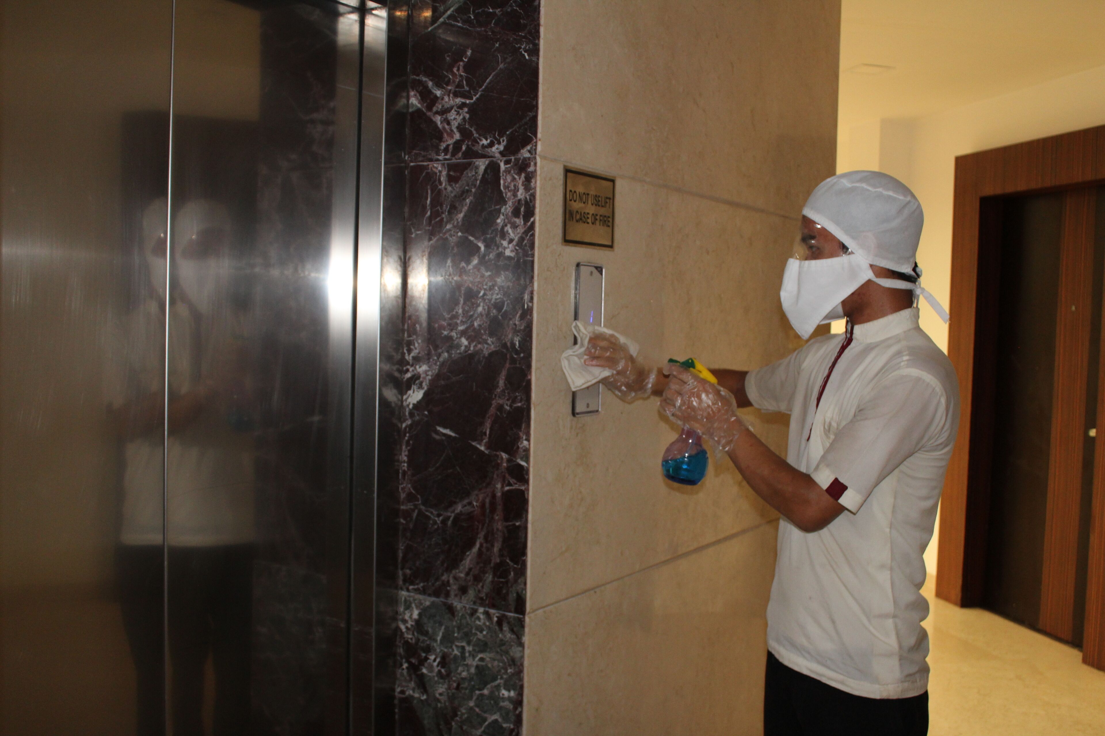 A person in a white uniform cleaning a marble elevator wall.