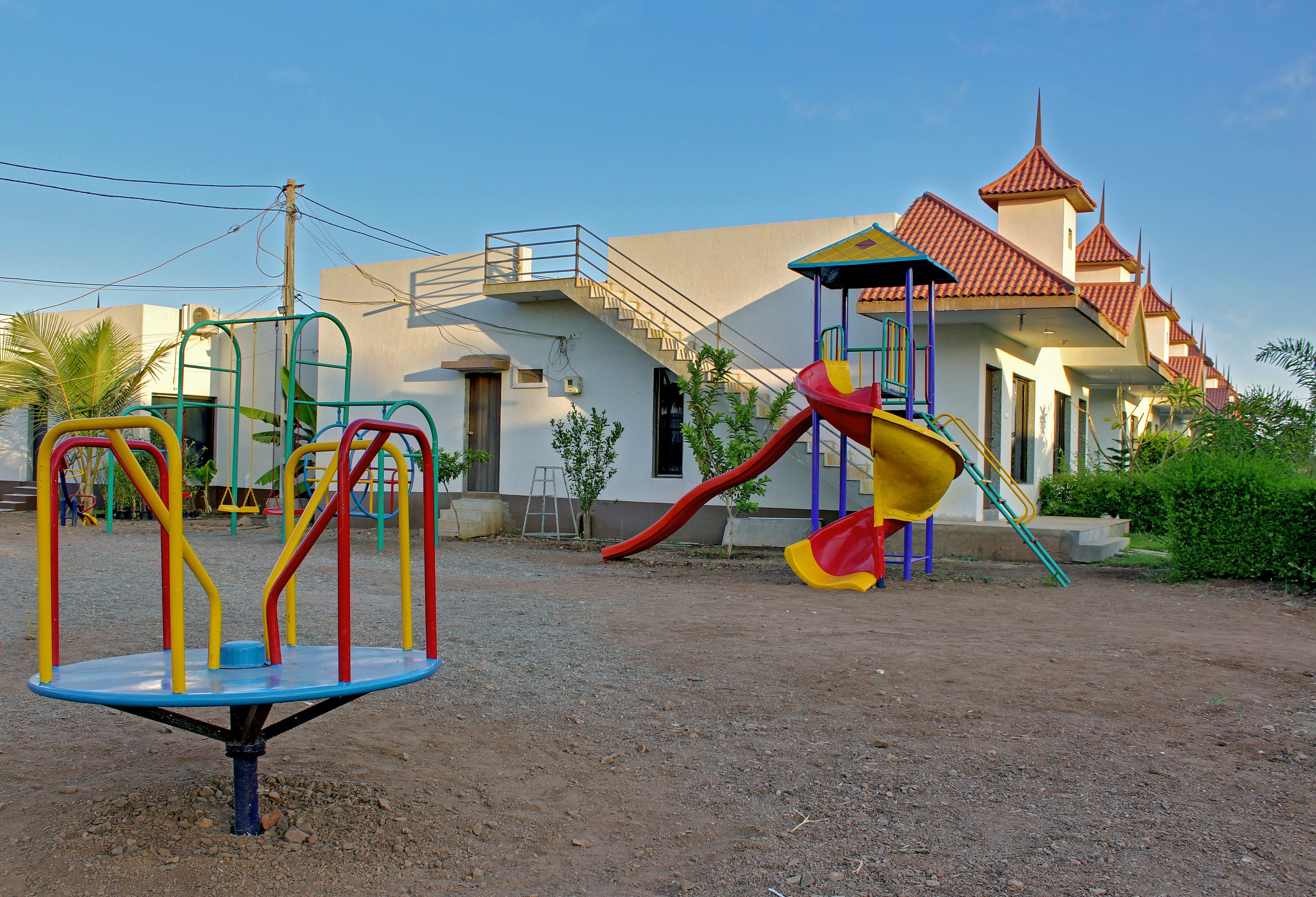 A playground with a slide and swings, a building with a red roof, and a staircase leading to an upper level.