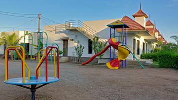 A playground with a slide and swings, a building with a red roof, and a staircase leading to an upper level.