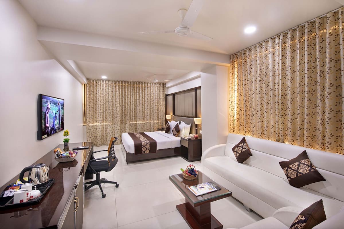 A hotel room with a bed, a sofa, a desk with a chair, a TV, and curtains.