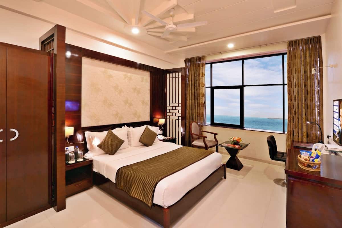 A hotel room with a large bed, a desk, a chair, a TV, and a window with a view.