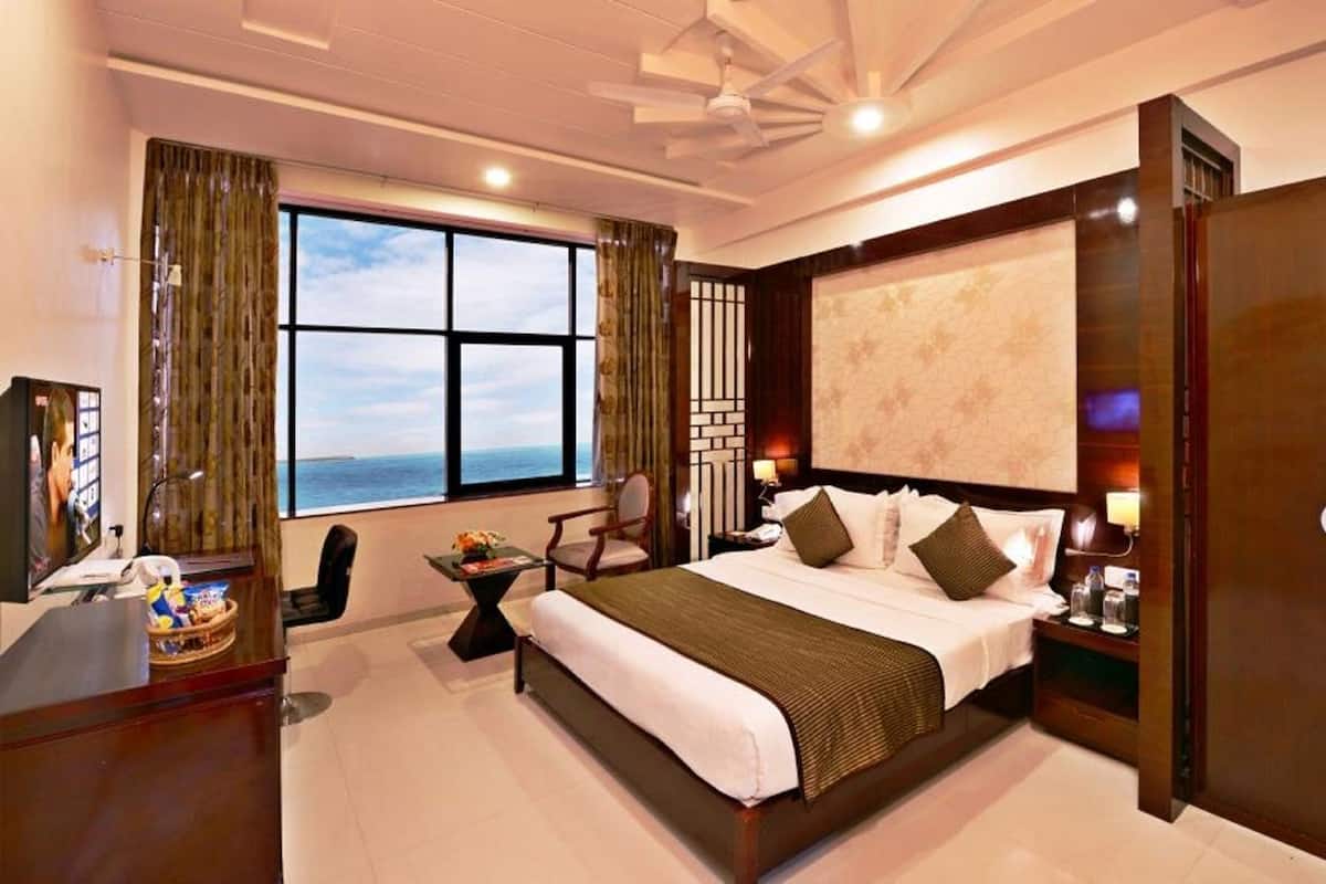A hotel room with a large bed, a desk with a computer, a chair, a TV, and a window with a view.