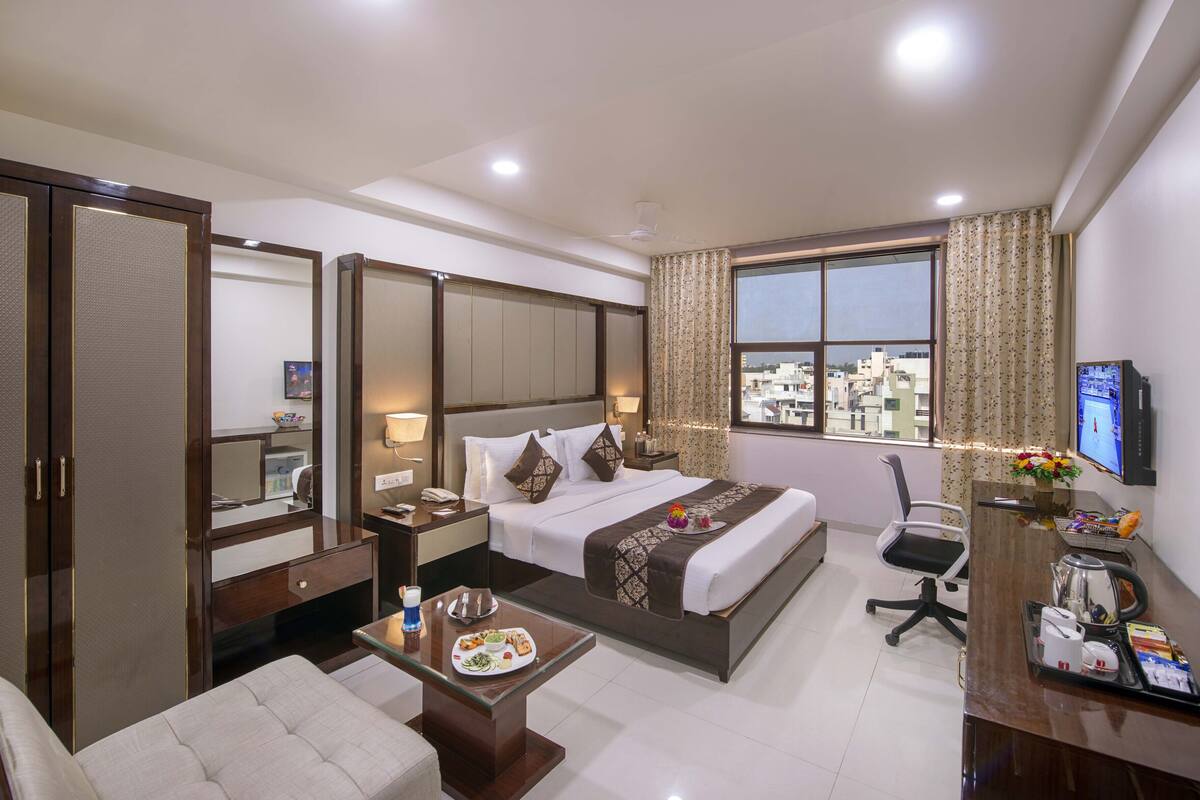 A hotel room with a bed, a desk, a chair, a TV, and a window with curtains.