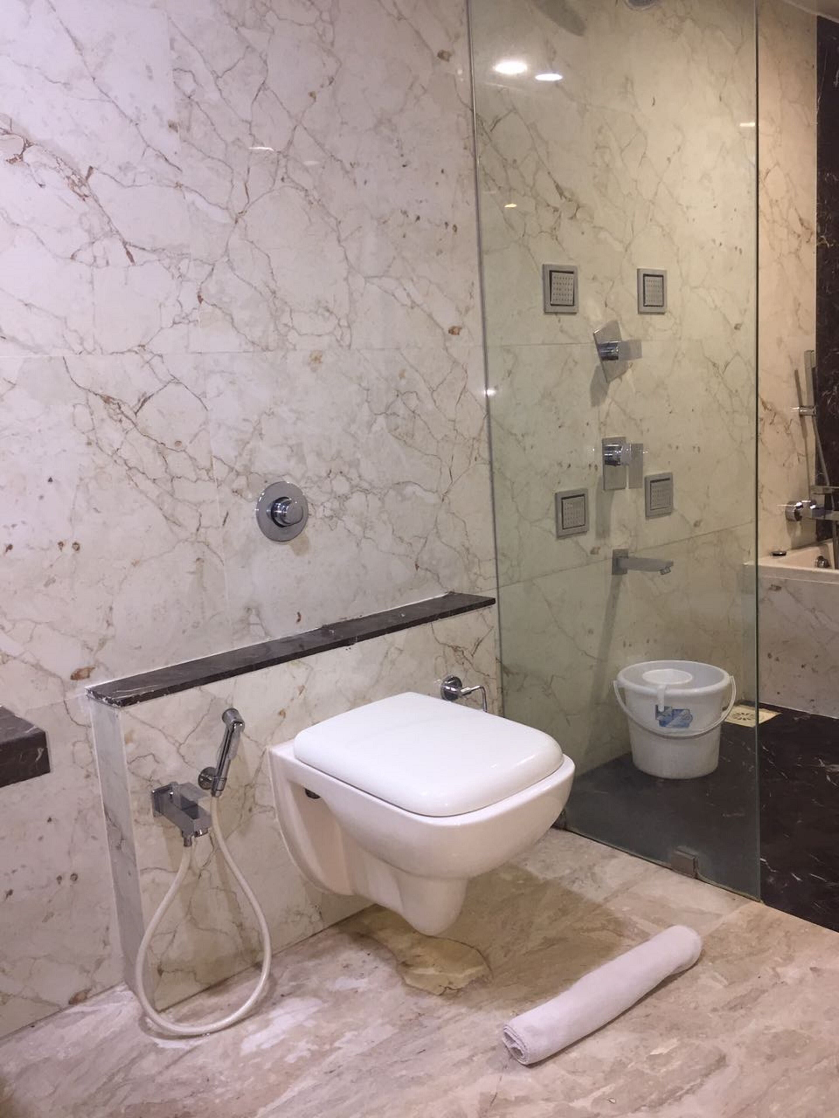 Een badkamer met een marmeren wand, toilet, douchegedeelte en een glazen douchecabine.