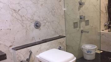 Een badkamer met een marmeren wand, toilet, douchegedeelte en een glazen douchecabine.