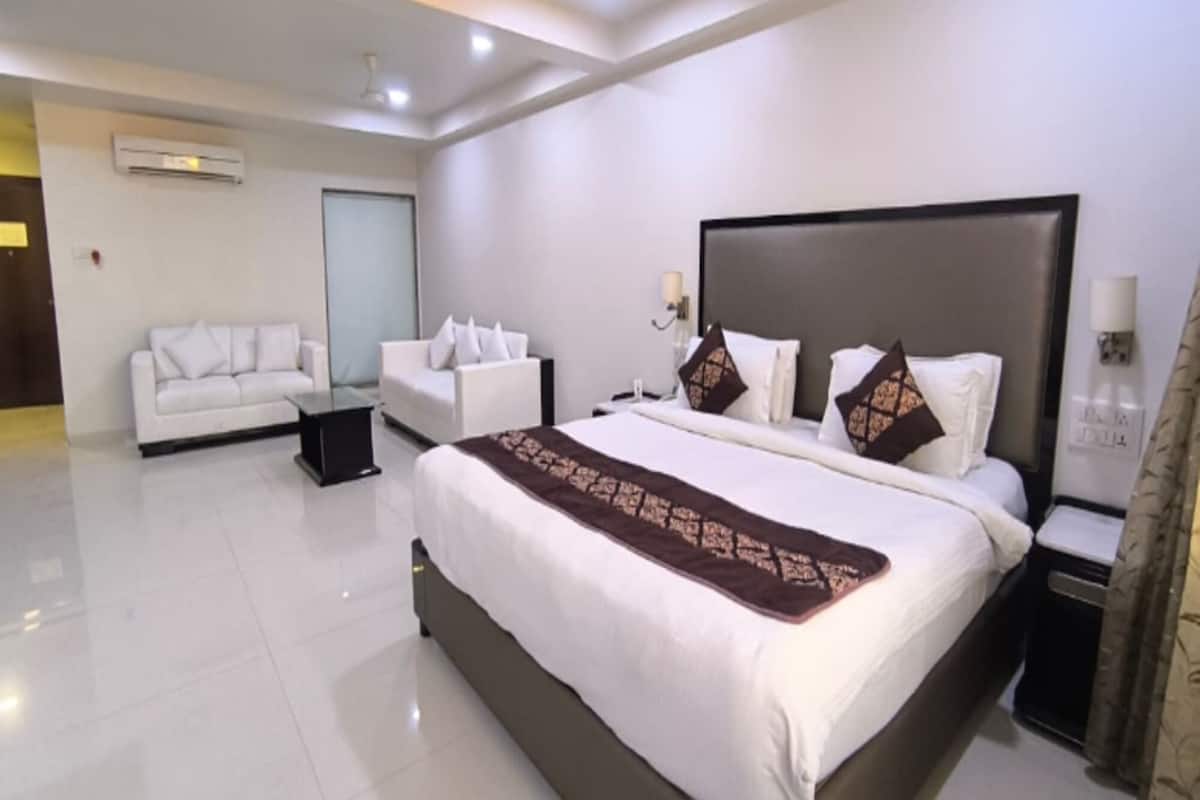 A modern hotel room with a large bed, two white sofas, a small table, and a nightstand.