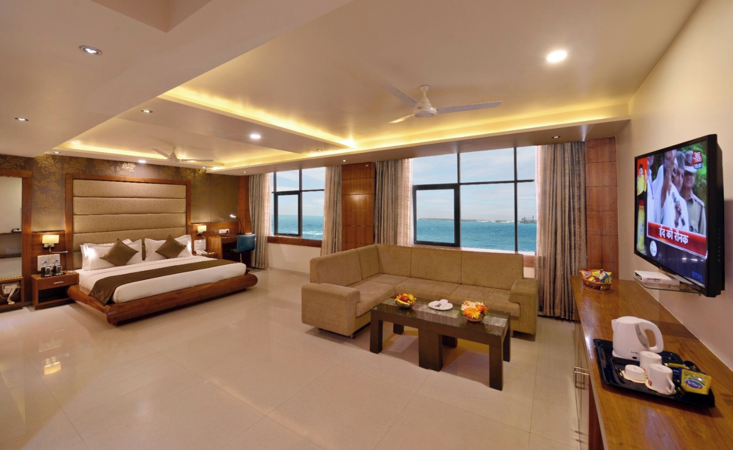Habitación de hotel con cama, sofá, televisión y vista al mar.