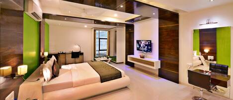 A modern hotel room with a large bed, a desk, a TV, and a seating area.