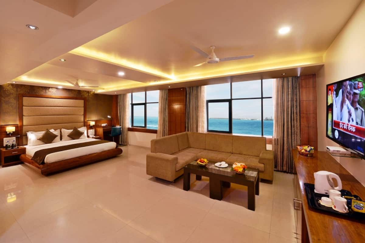 A hotel room with a bed, sofa, TV, and a view of the sea.