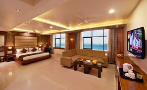 Una camera d'albergo con un letto, un divano, una TV e vista sul mare.
