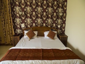 A neatly made bed with a brown bedspread, two decorative pillows, and a floral wallpapered headboard. - Skyview Holiday Home (Chandigarh)