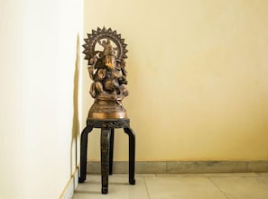 A statue on a pedestal in a corner of a room with plain walls and a tiled floor. - Skyview Holiday Home (Chandigarh)
