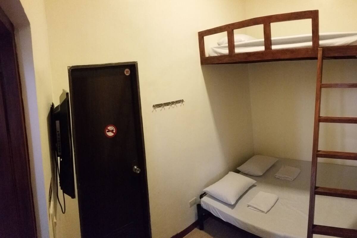 A small, compact room with a bunk bed, a door with a no-smoking sign, and a small shelf with a few items.