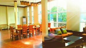A spacious room with a dining area featuring wooden chairs and a table, large windows with a view of greenery, and a sofa with patterned cushions. - The Inn at Calayo (Nasugbu)