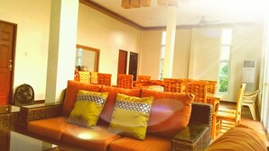 A living room with a sofa, wooden chairs, a fan, and a window with curtains. - The Inn at Calayo (Nasugbu)