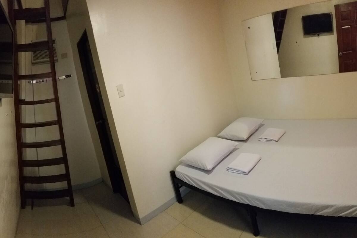 A bedroom with a bed, pillows, a ladder, and a mirror.