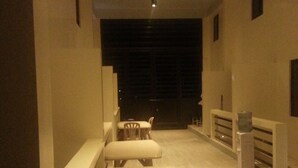 A corridor with a dining area featuring a table and chairs, a small stool, and a trash bin. - The Inn at Calayo (Nasugbu)
