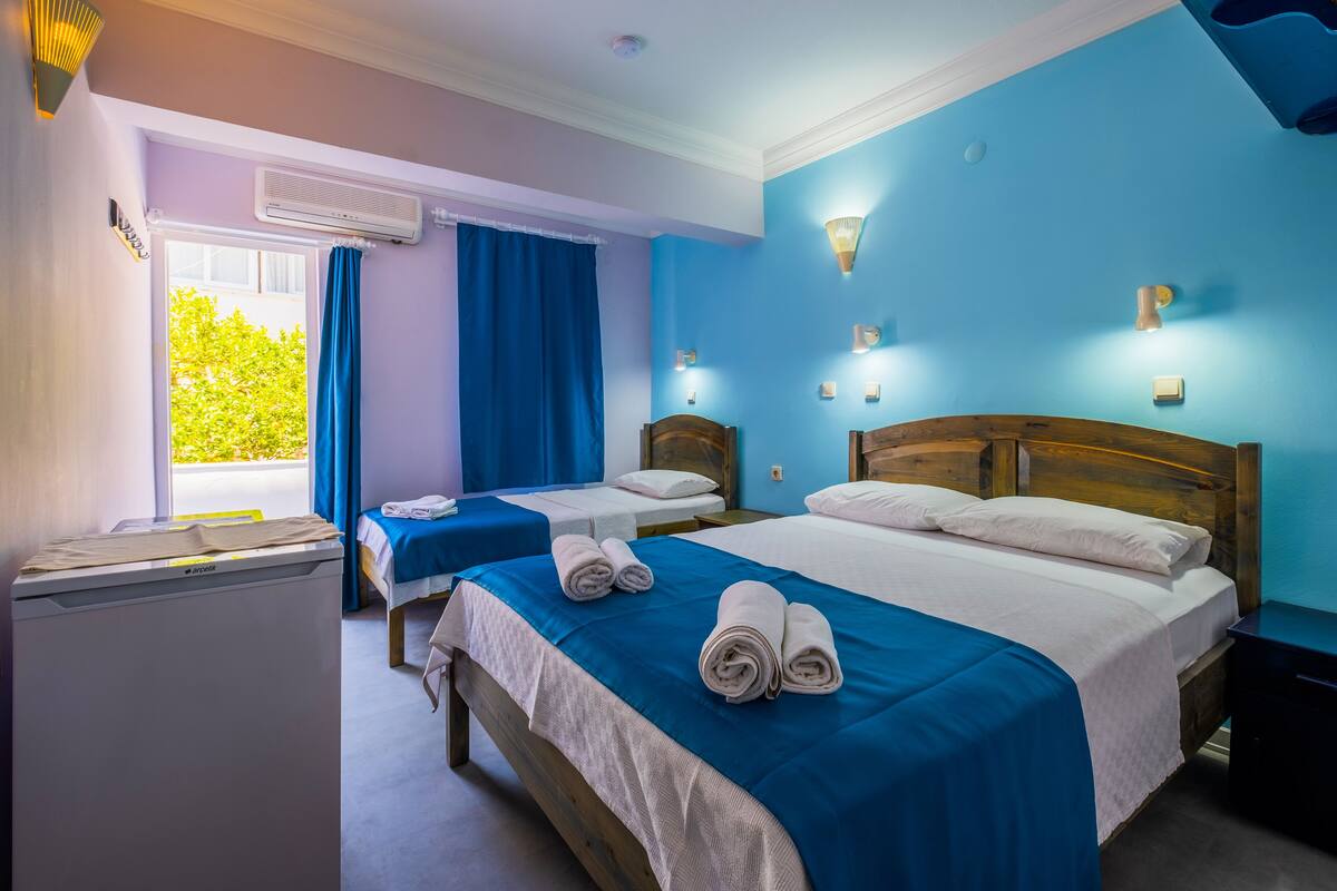 A hotel room with two beds, a washing machine, and a window with curtains.