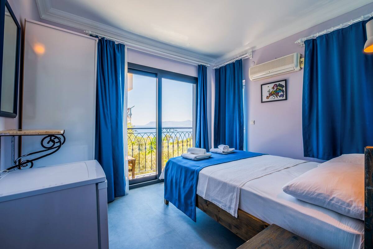 A hotel room with a balcony, a bed, a desk, and a window with curtains.