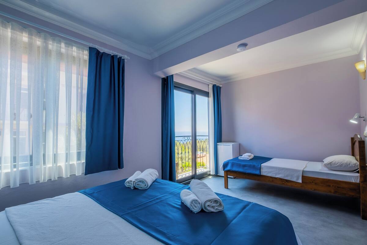 A hotel room with two beds, a balcony, and a view of the outdoors.