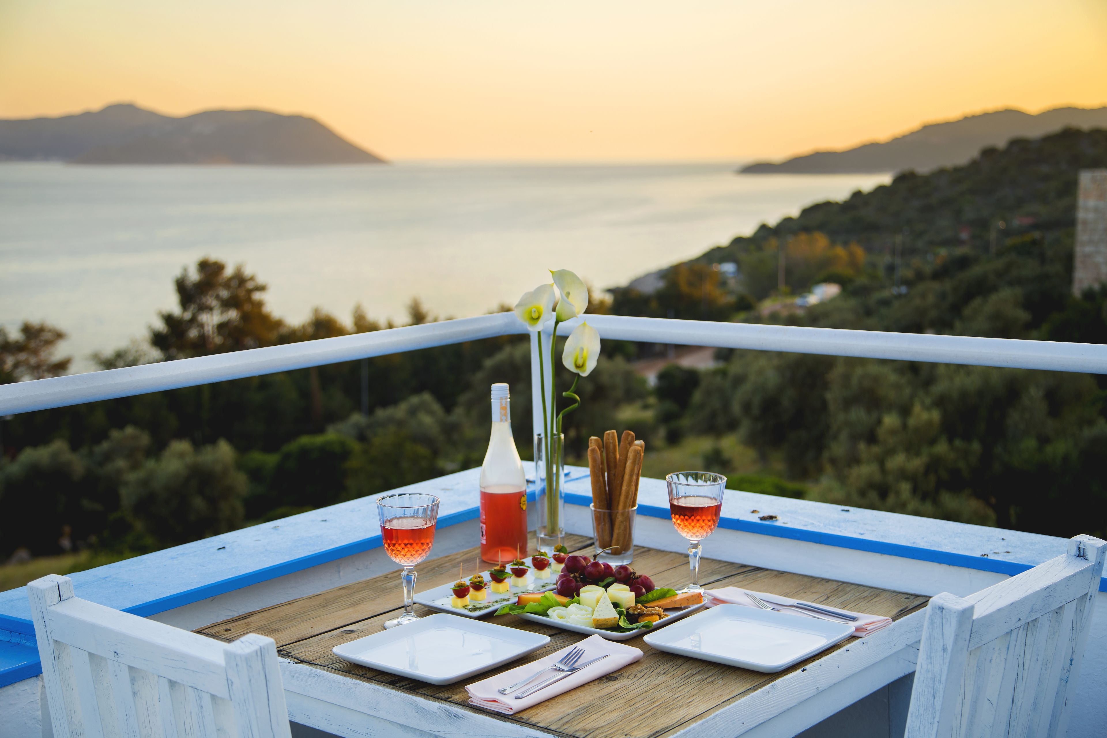 A table set for a meal with a scenic view of the sea and hills in the background.