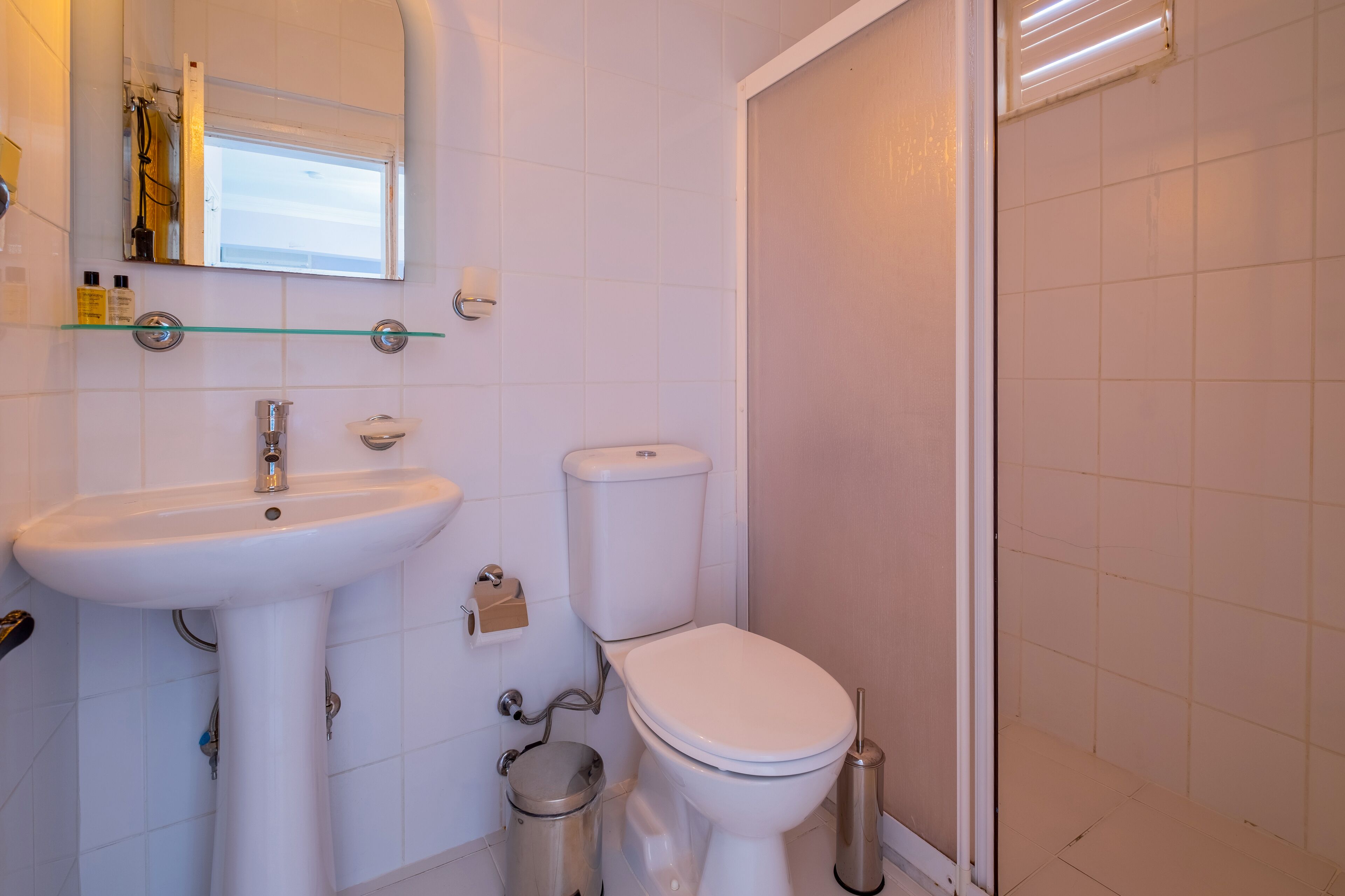A bathroom with a white sink, toilet, and a glass shelf above the sink.