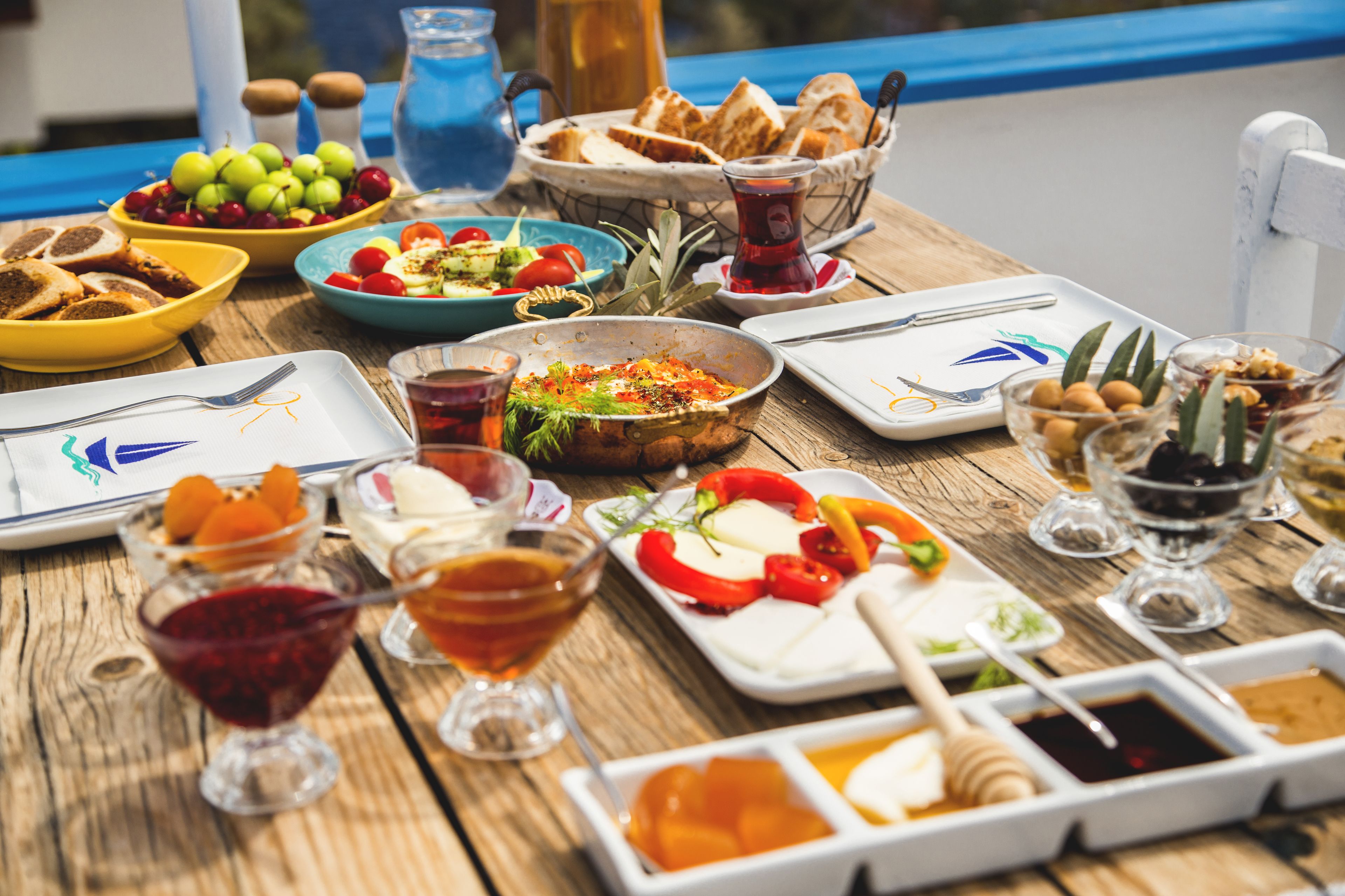 Une table en bois sur laquelle sont disposés divers aliments et boissons, notamment des assiettes de fromage, des olives et un bol de raisins.