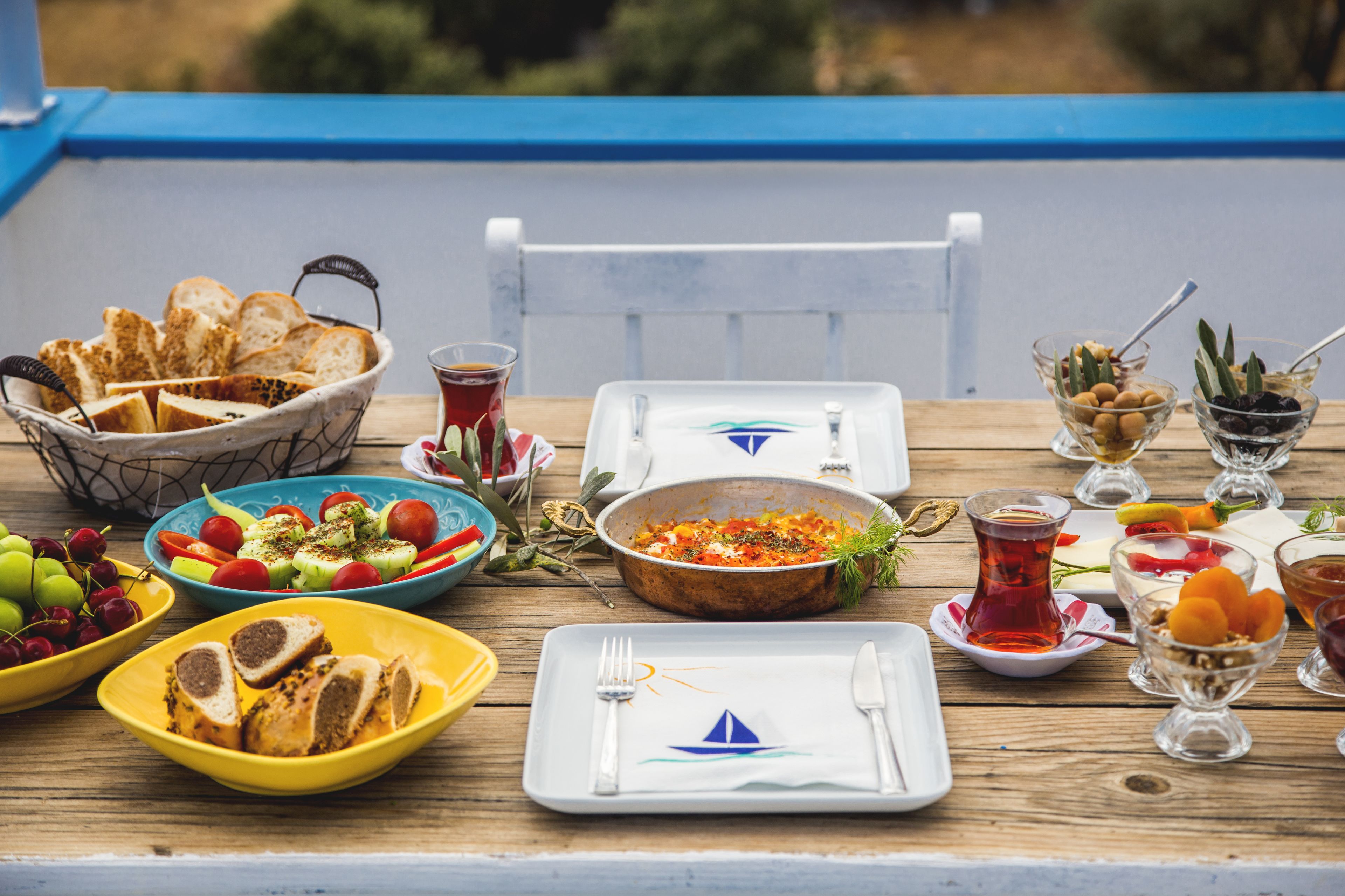 A wooden table set with various dishes, including bread, salad, and fruit, and a glass of tea.