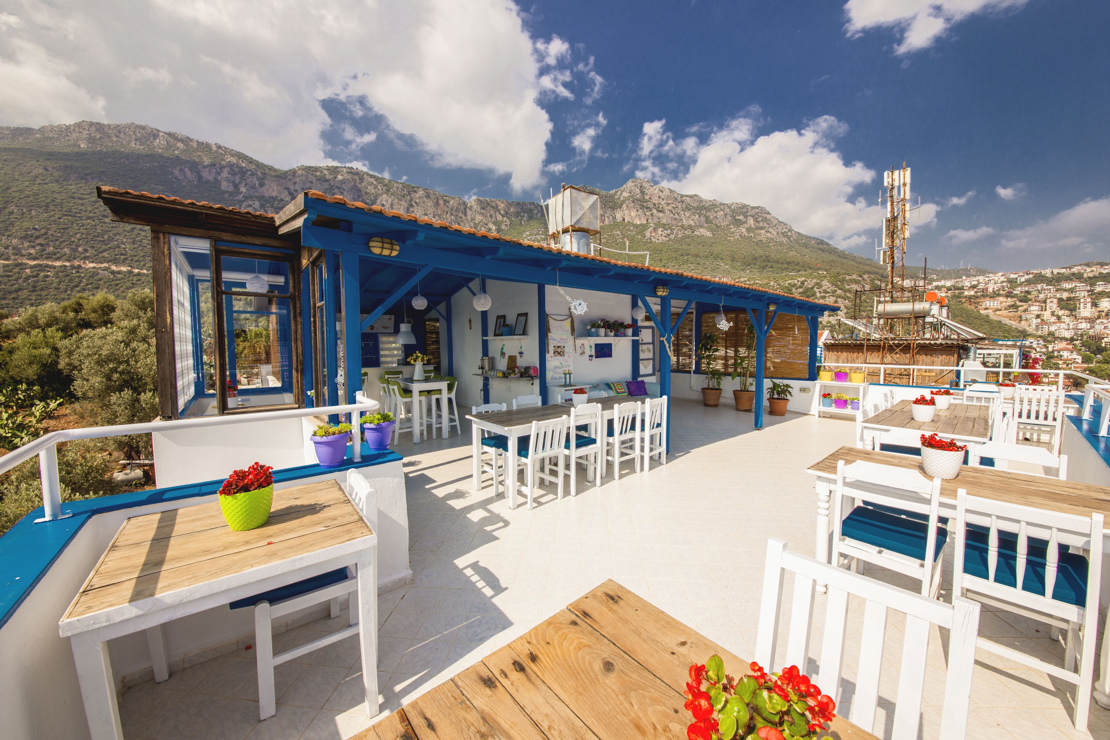 A seaside restaurant with outdoor seating, a mountain backdrop, and a view of the city.