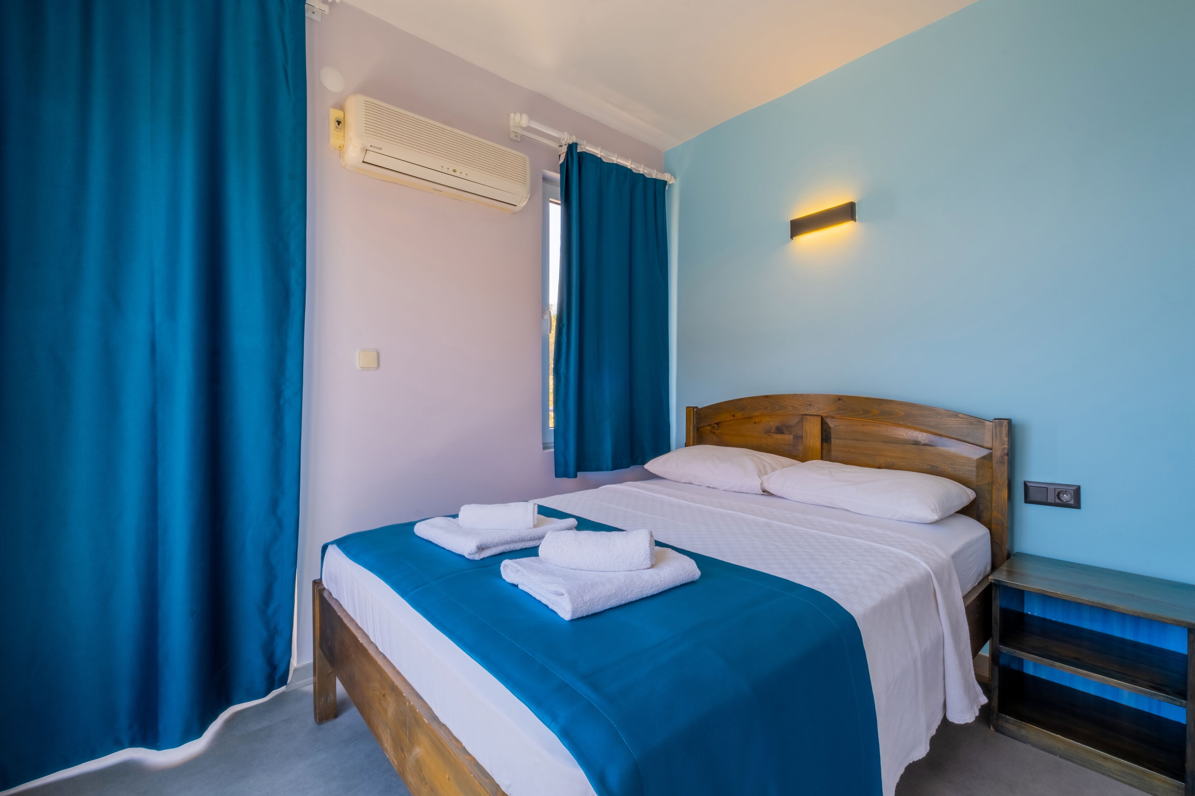 A bedroom with a wooden bed, blue curtains, a white bedspread, and a nightstand with a lamp.