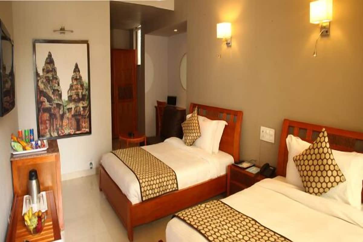 Quarto de hotel com duas camas, cabeceira de madeira, mesa de cabeceira, luminária na parede e um quadro de um templo.