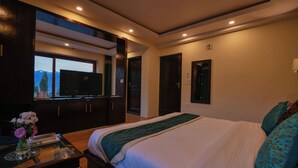 A hotel room with a large bed, a TV, and a view of mountains through a window. - Hotel Ladakh Inn (Leh)