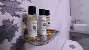 A bathroom with a shower area, a sink, and a shelf holding three bottles of Hotel Ladakh products. - Hotel Ladakh Inn (Leh)