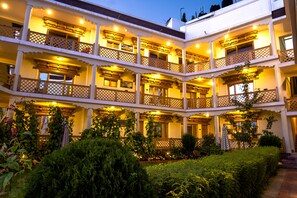 Un hotel de varios pisos con balcones, un jardín y una fachada bien iluminada.