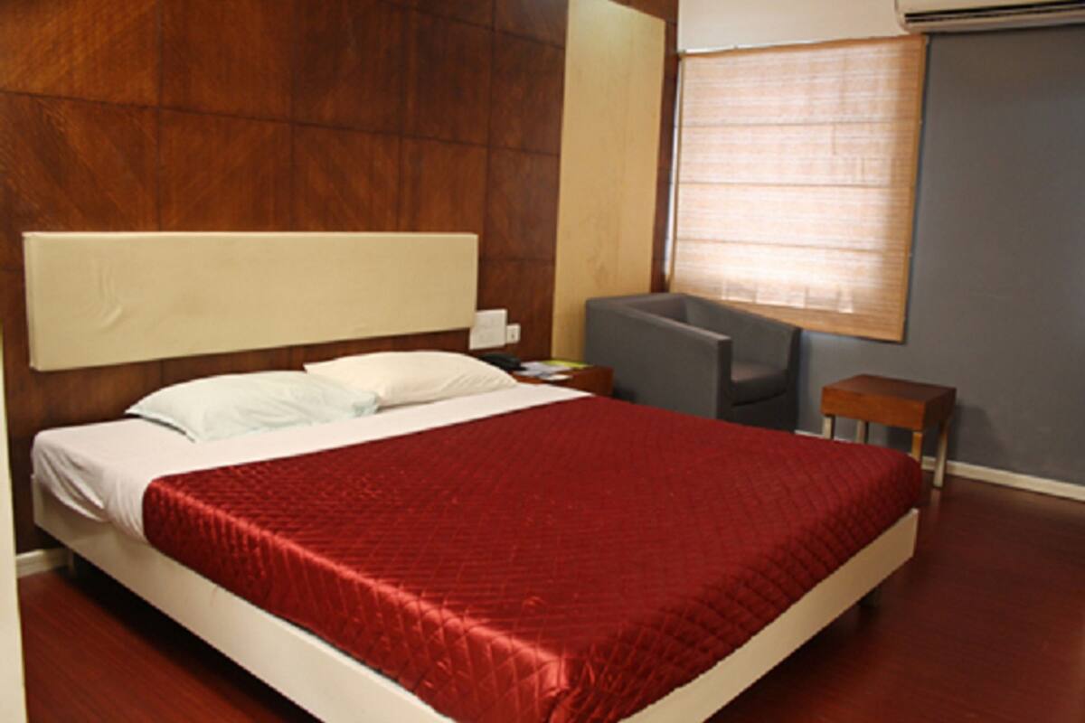 A hotel room with a large bed, a bedside table, a chair, and a window with blinds.