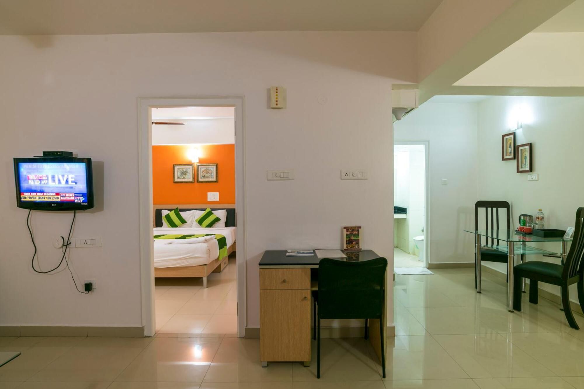 Habitación de hotel con cama, escritorio, silla, televisor y zona de comedor con sillas y mesa.