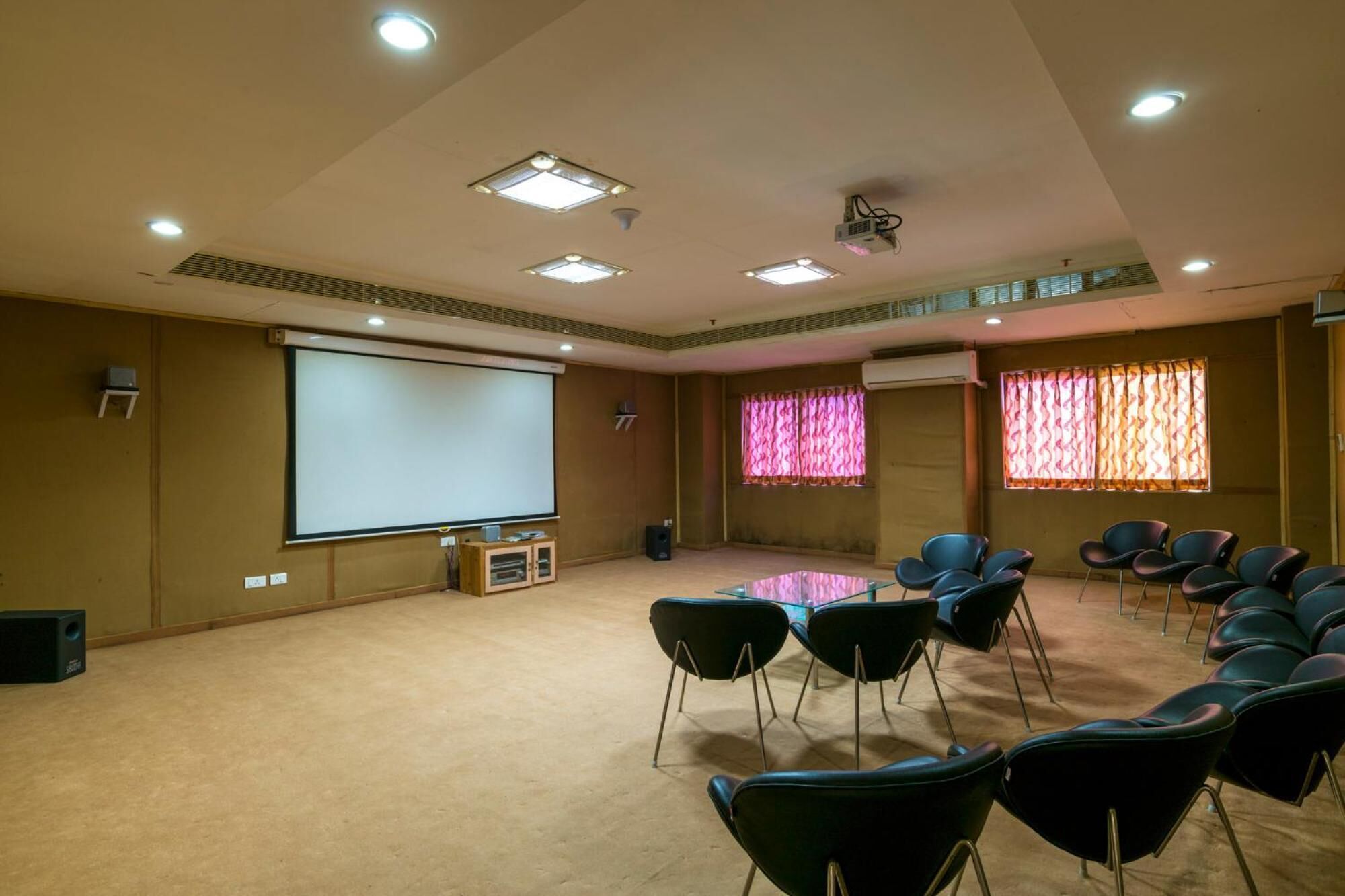Un salón de conferencias con una pantalla grande, varias luces en el techo y filas de sillas.