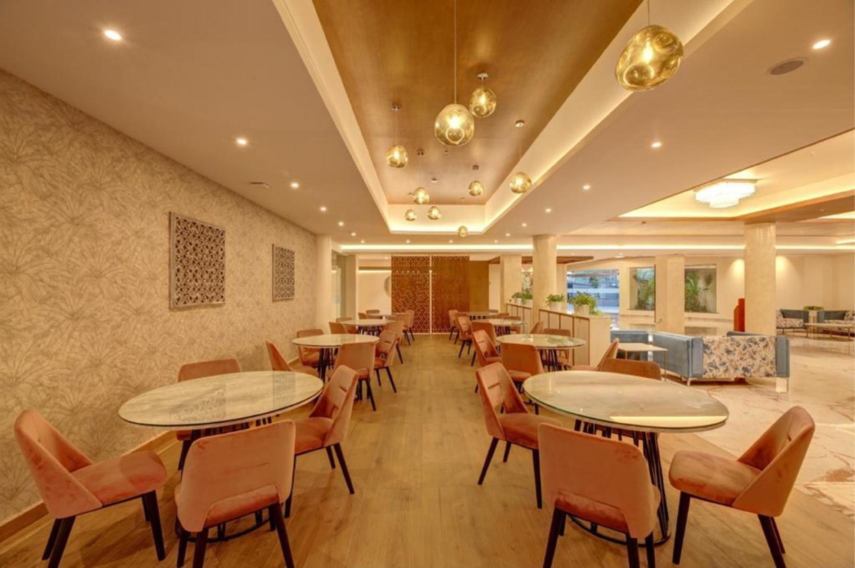 A spacious dining area with round tables and orange chairs, a wooden ceiling, and decorative wall panels.