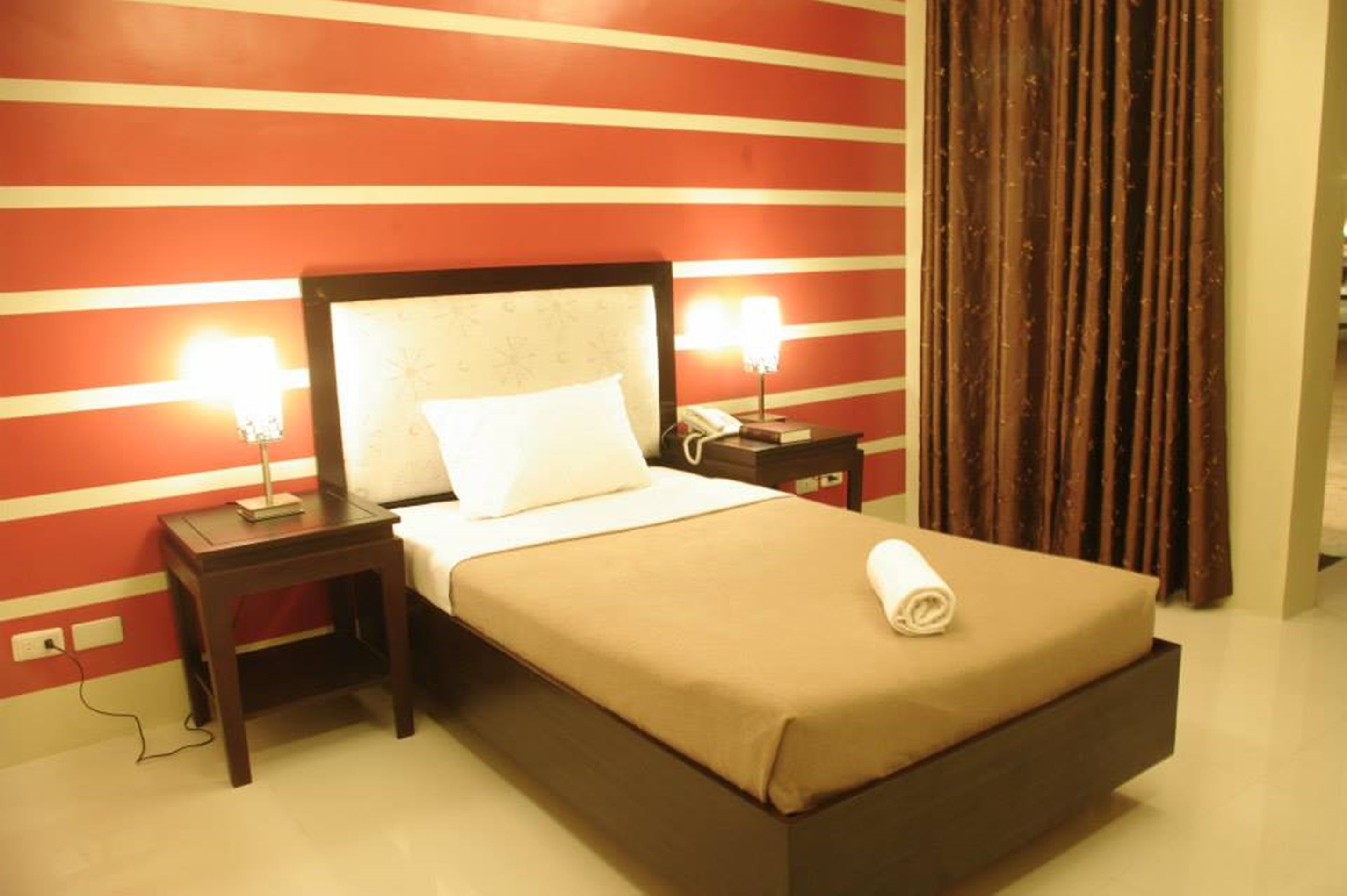 A hotel room with a bed, two bedside tables, a nightstand, a lamp, and a curtain.