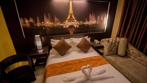 Une chambre d’hôtel équipée d’un lit, d’un canapé, d’un fauteuil, d’une table de chevet et d’un grand téléviseur fixé au mur, qui diffuse une image de la Tour Eiffel.