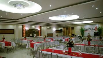 Un salón de banquetes con mesas redondas, manteles rojos y sillas blancas.